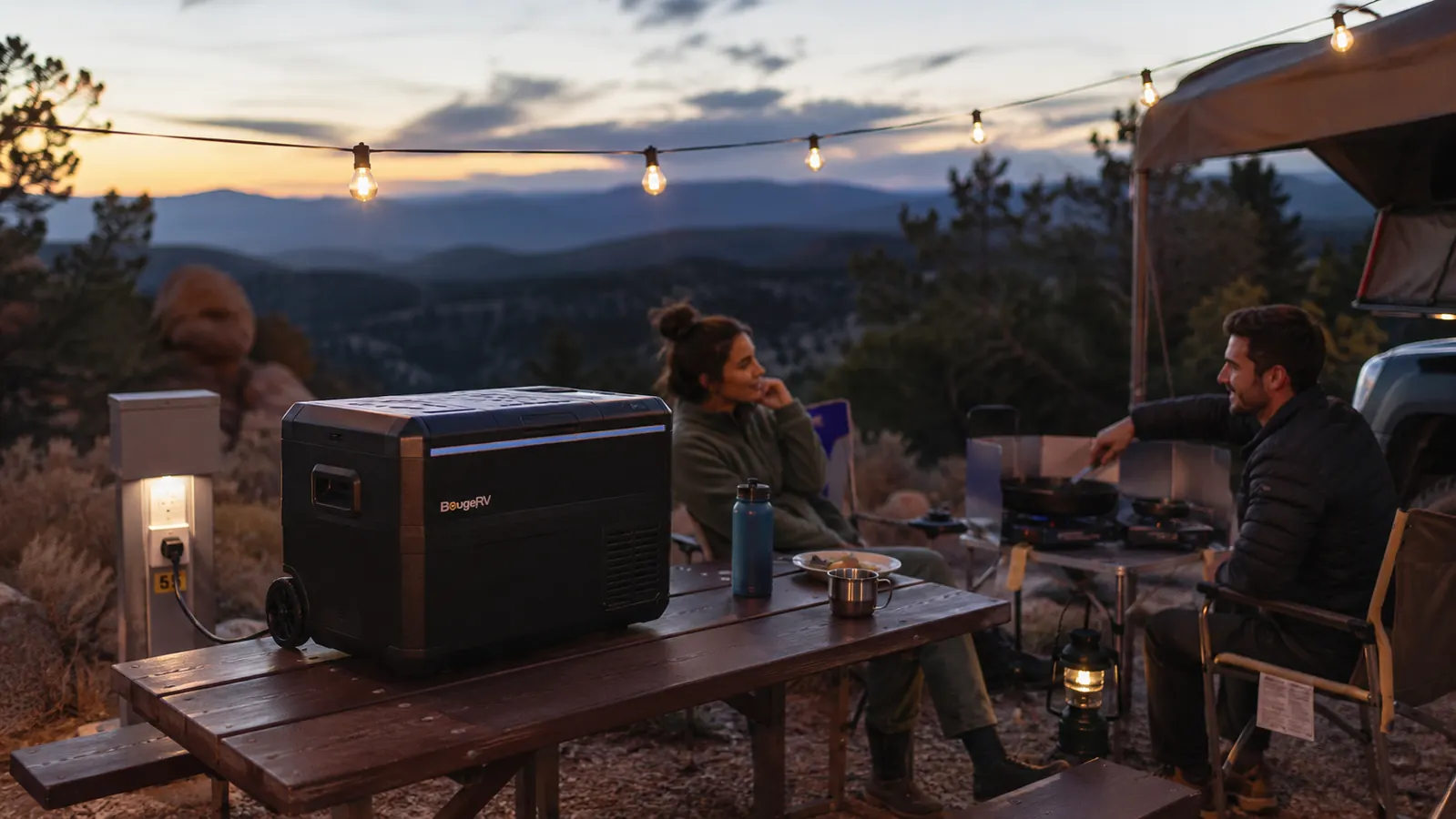 A 12V fridge running on wall power at a campground picnic table at dusk