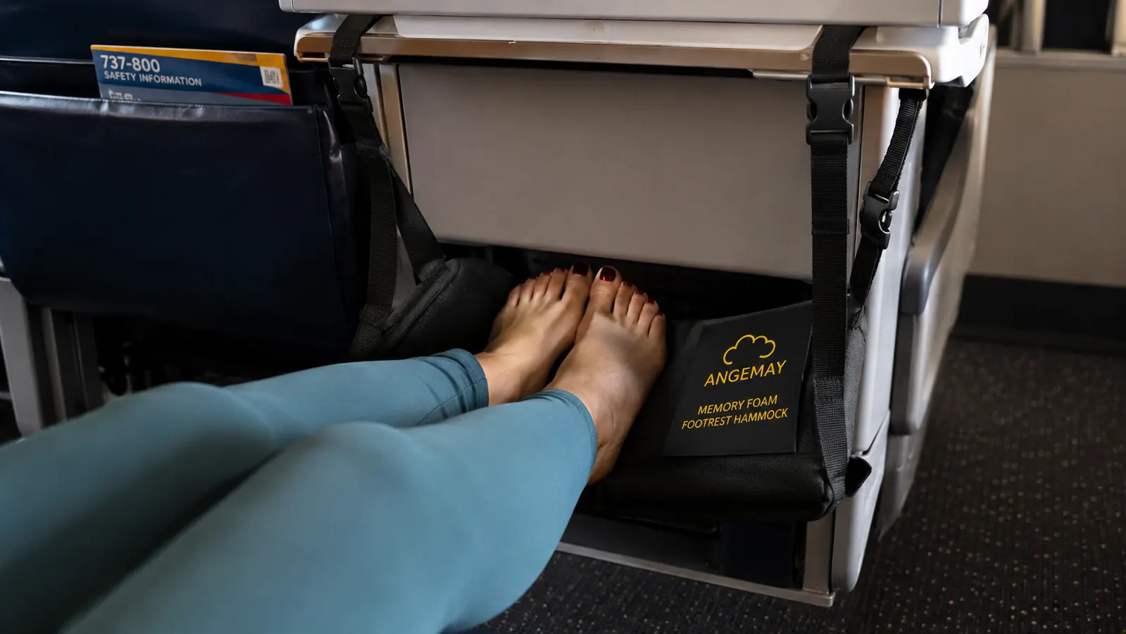 Memory foam airplane footrest hanging from a tray table hook with feet resting on top of it