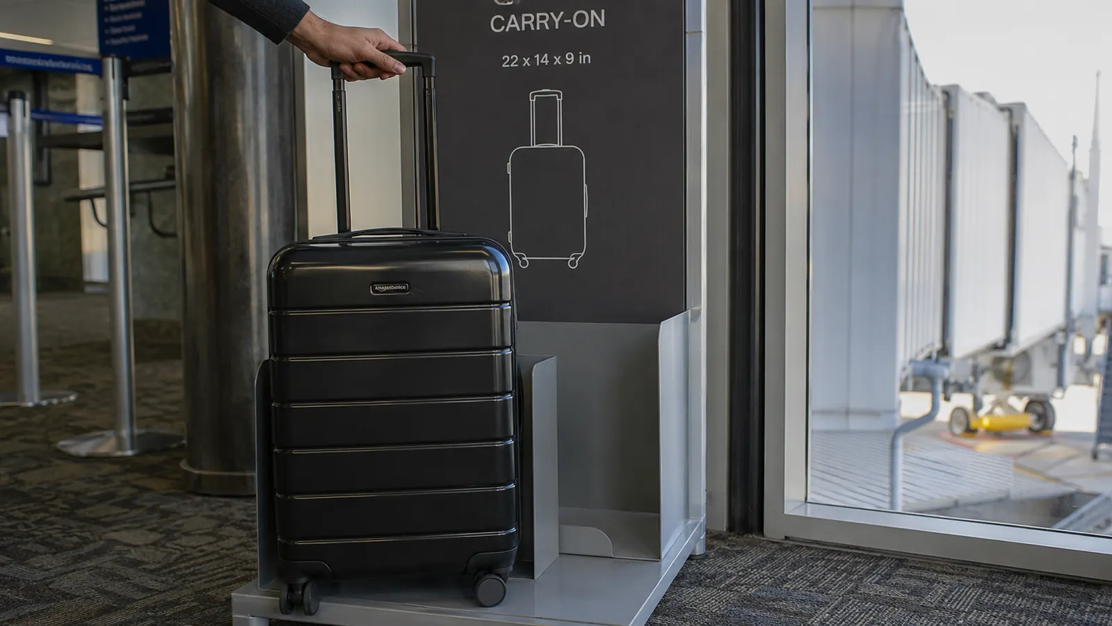 Hand extending the telescoping handle of the Amazon Basics carry-on next to an airline seat sizer frame