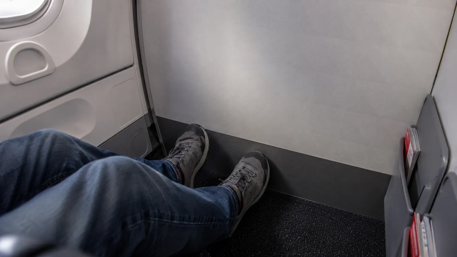 Passenger's feet dangling with no footrest attached near a bulkhead wall on an airplane