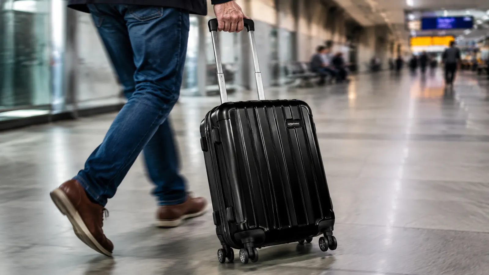 Close-up of a hand pulling the telescoping handle of a black hardside carry-on through a busy airport concourse