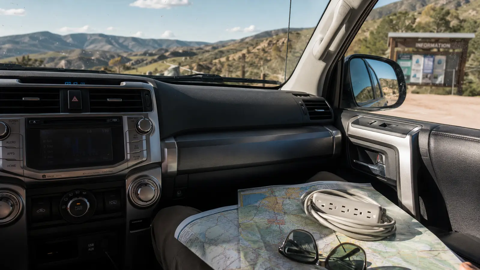 A travel power strip resting in the center console of a Toyota 4Runner next to a road atlas and sunglasses