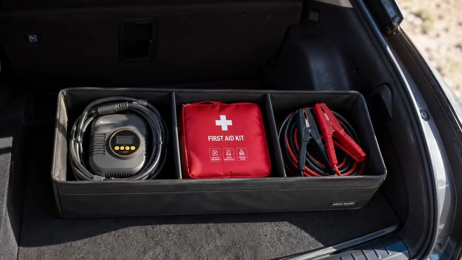 A compact tire inflator packed neatly into a cargo area storage bin next to a first aid kit and jumper cables